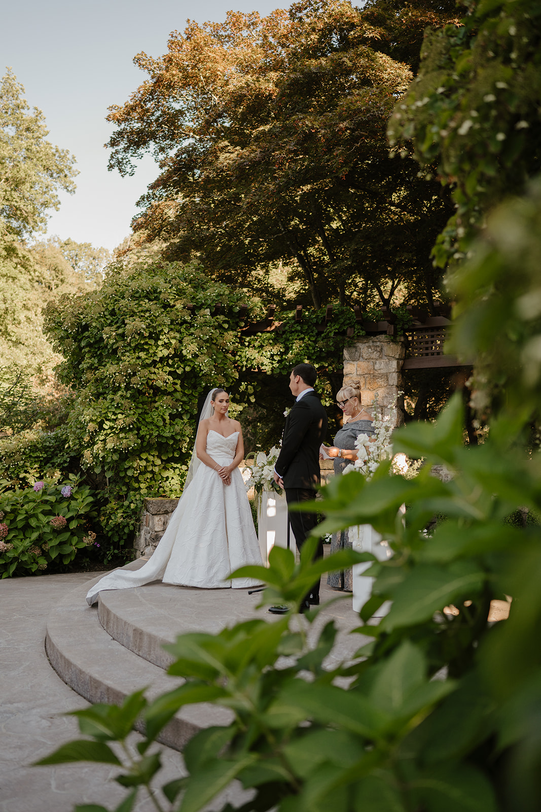 Bride and groom standing at the stone altar during their ceremony, framed by green leaves in the foreground.